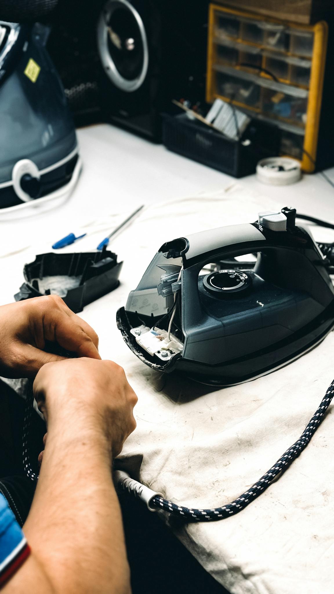 Hands working on repairing an iron in a workshop. Tools and parts are visible.